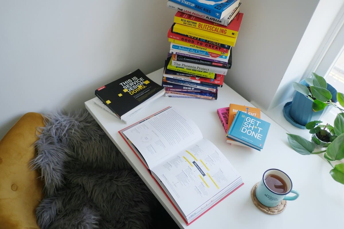 自己投資やビジネスに関する書籍が積まれた机と、開かれたノートにメモが記された学習風景。お金や考え方を整える大切さを示す一棟マンション投資の事前準備イメージ。