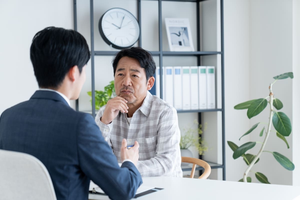 不動産投資に関する相談を真剣に受ける中年男性と若い相談者。判断と行動の分岐点で悩みながらも前向きな選択を模索する場面。